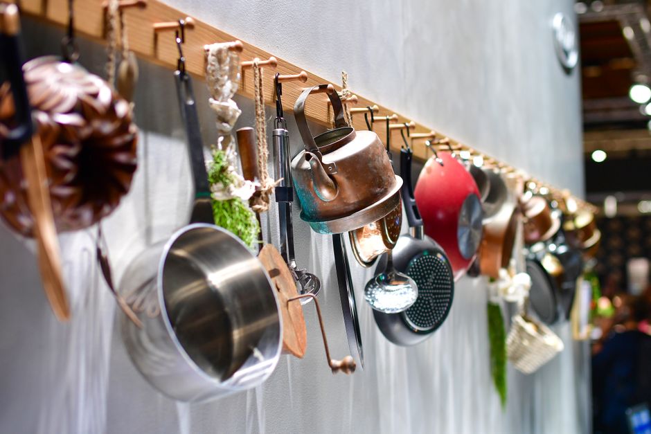 A rustic kitchen setting with various cookware hanging on a wooden rack indoors.